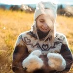 Smiling woman outside in nature wearing a matching white knitted set from “Okstind” with winter hat and mittens.