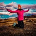 Colorful woman jumping of joy from being outside in beautiful nature wearing an orange winter hat from “Okstind”.