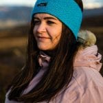 Smiling woman outside in nature with bright blue knitted headband from “Okstind”.