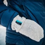 Knitted white mittens from “Okstind” matching with the blue jacket the model is wearing.