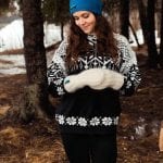 Smiling woman outside in nature with bright blue knitted headband from “Okstind”.