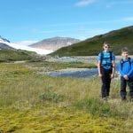 Three young kids with matching blue clothes smiling in beautiful surroundings in the mountain during summer.