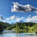 Shining clear water surrounded by green and lively nature with great mountains in the background on a blue-skied summer day.
