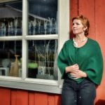 Goldsmith, Merete Mattson, outside in front of her red store with her work hanging in the window and another on her neck.