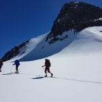 Skiers in an open and white mountain landscape passing a big mountain on a blue-skied day.