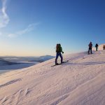 Several skiers climbing a snowy mountain, while having a view over the fjord and other mountains in the horizon.