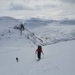 Skiers climbing a steep and snowy mountain with a great view over other mountains in the horizon.