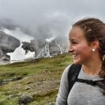 Happy young girl hiking in Okstindan on a cloudy day with snow and a small mountain lake seen in the background.