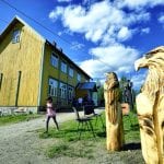 Young girl walking in front of the old yellow schoolhouse bakery in Bleikvasslia and the eagle sculptures standing outside.