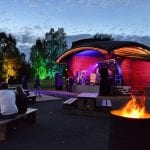 Concert at Parkrock festival at night with the stage lighted up in different colors with people watching, next to a fire.