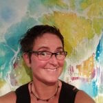 Portrait of the smiling and buoyant artist, Yvonne in front of a colorful painting.