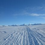 View of mountains in the horizon from a snowmobile track surrounded by all snowy whiteness.