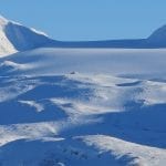 View of the cabin, Rabothytta, from snowmobile tracks on another mountain in completely white surroundings.