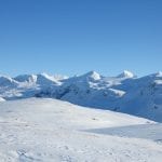 Snow-white view in all directions seen from snowmobile tracks in the mountains with the Okstindan mountains in the back.