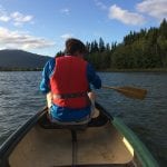 Young boy with a red life vest sitting in front of the canoe paddling down the river, Røssåga on a blue-skied day.