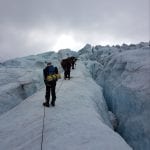 People climbing a steep glacier filled with crevasses, together with ropes between each other.