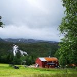 Mastervika Farm surrounded by green nature and waterfalls, and a tree-tent hanging in the trees next to the farm.