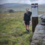 Girl standing next to a sign in the mountains telling the story of the sami Stor Nila