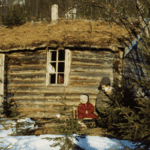 A child in red clothes and a man sitting outside of a hut.