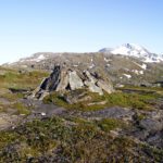 A mountain landscape with white mountain in the background and a pile of rocks in the fore ground.